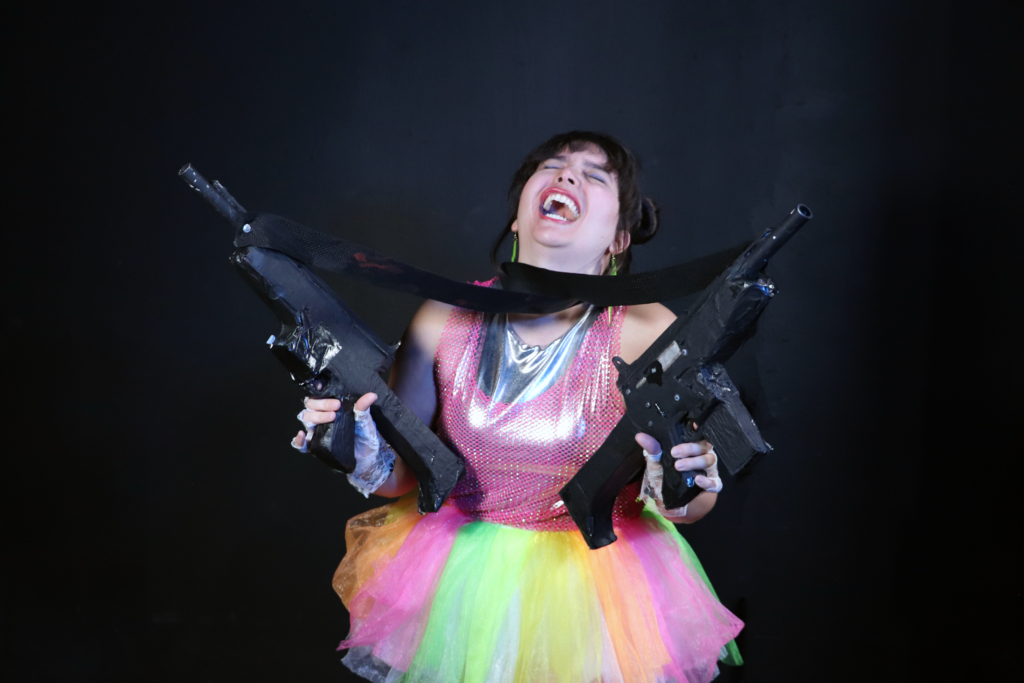 Woman in multicolor neon tutu holding two semiautomatic weapons and laughing